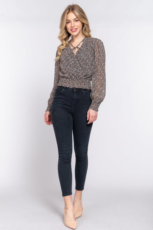 Woman wearing black floral smocked chiffon blouse with long sleeves and tie detail, paired with dark jeans.