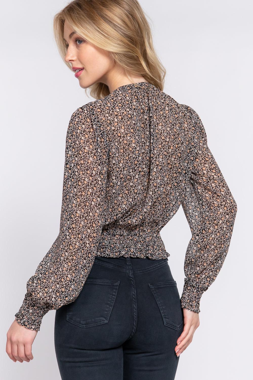 Woman wearing black floral print chiffon blouse with smocked waist and long sleeves, back view.