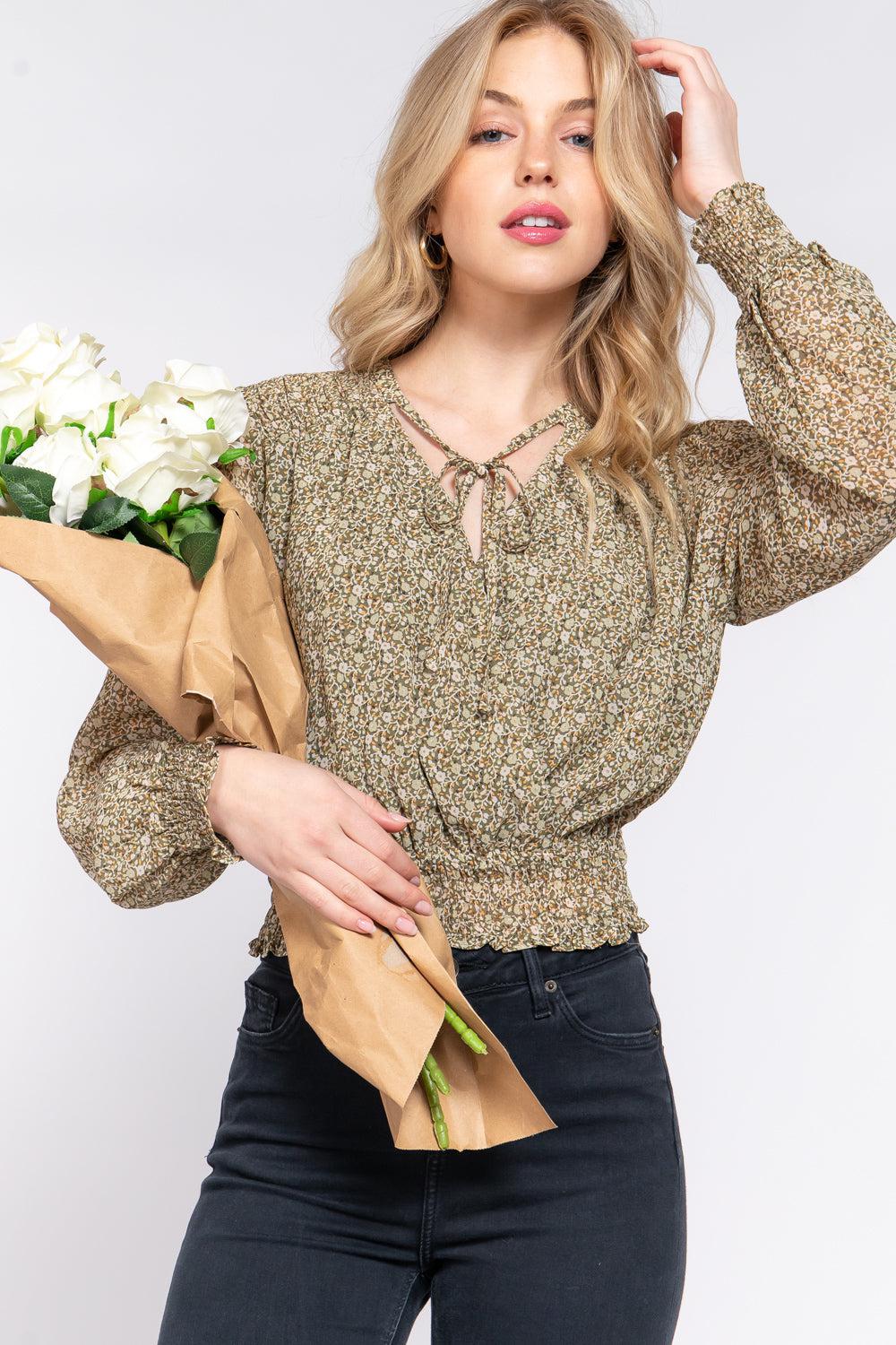 Woman wearing an olive floral chiffon blouse holding white flowers in paper wrap.