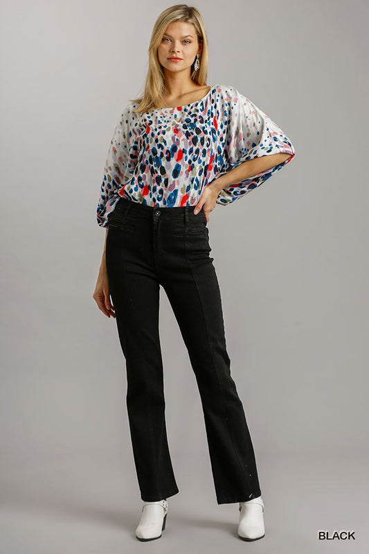 Woman wearing black straight cut denim jeans with pockets and a colorful patterned top.