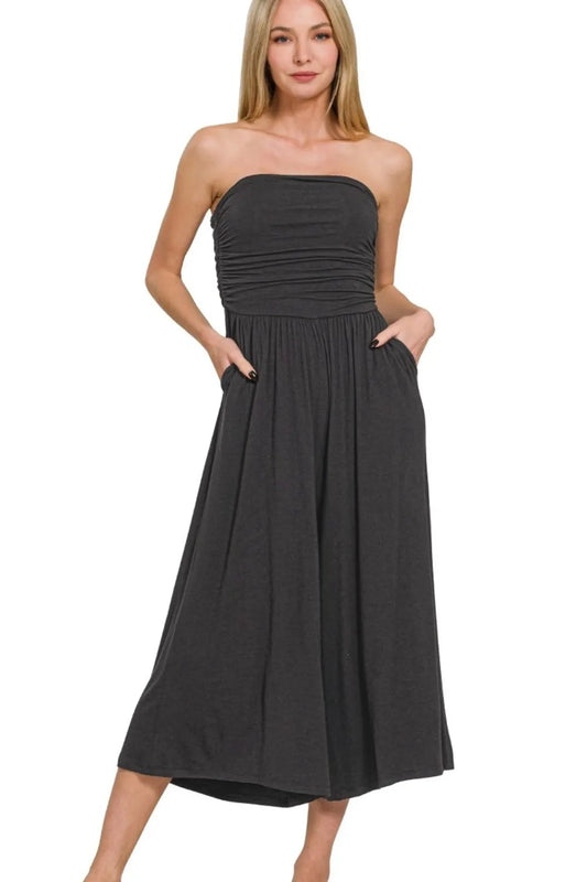 Woman in charcoal gray strapless midi dress with ruched bodice and pockets, standing against white background with hands in pockets.
