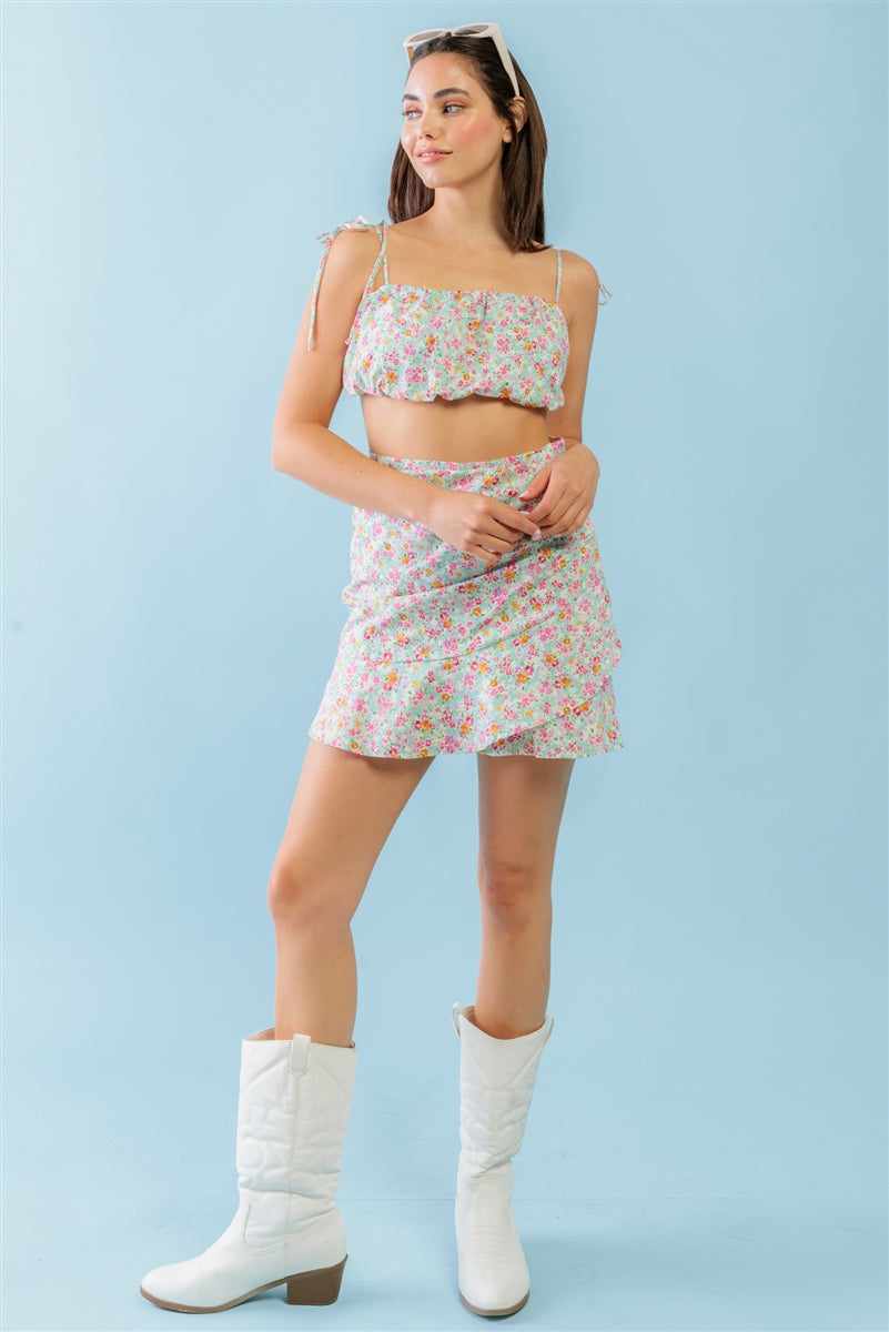 Woman wearing a mint fuchsia floral strappy crop top and high waist mini skirt set with white boots, featuring a trendy girlish look.