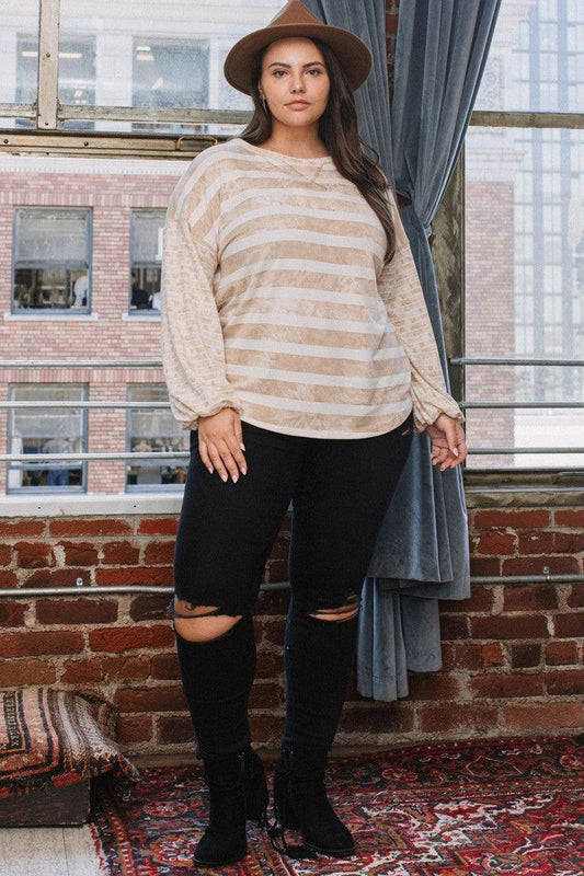 Woman wearing a stripe printed taupe French terry top with round neckline and contrast sleeves, styled with a hat and black jeans.