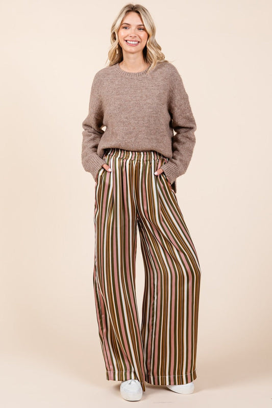 Woman wearing striped satin wide leg pants with elastic waist and pockets, paired with a cozy knit sweater.