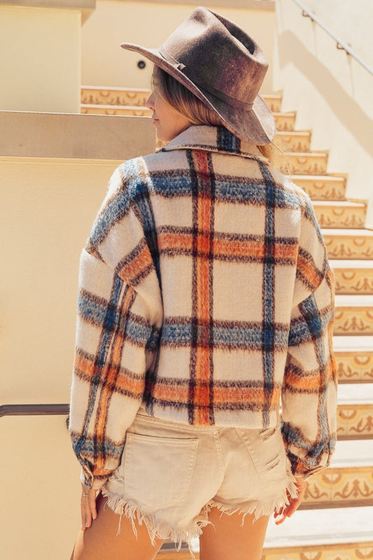 Woman wearing an ivory multi-color brushed plaid crop jacket with pockets, featuring a buttoned front and standing outdoors.