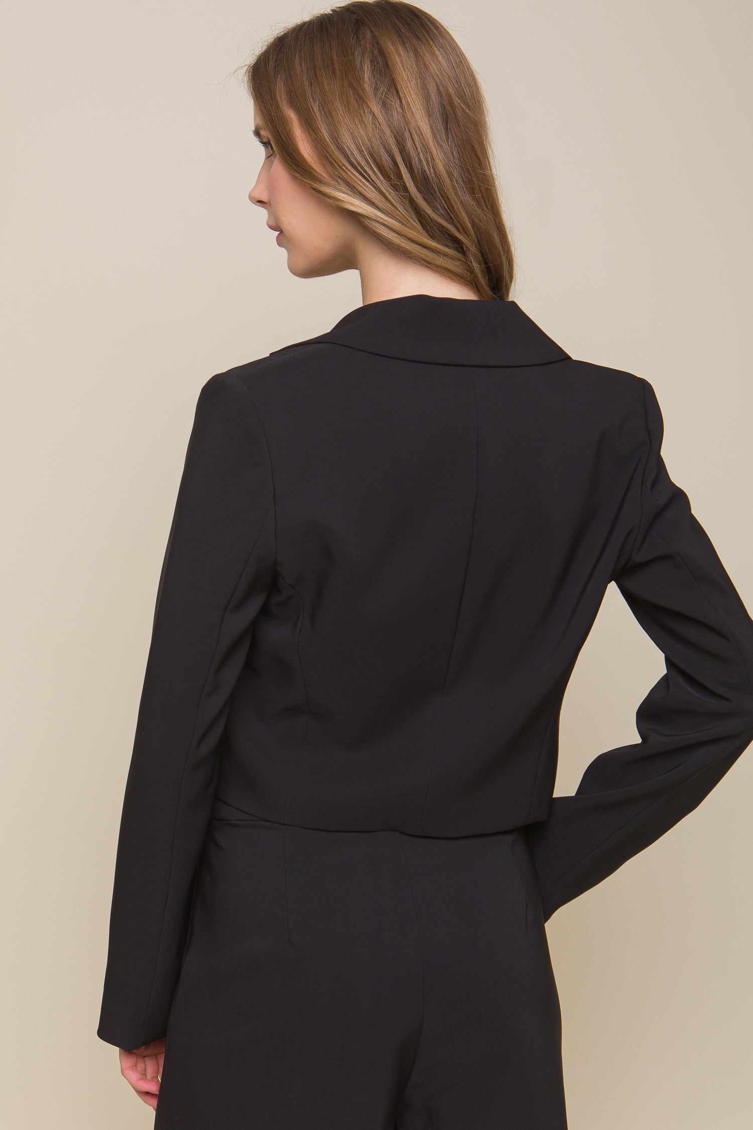 Woman wearing a black button crop blazer, made of 95% polyester and 5% spandex, showcasing the back view of the sleek jacket.