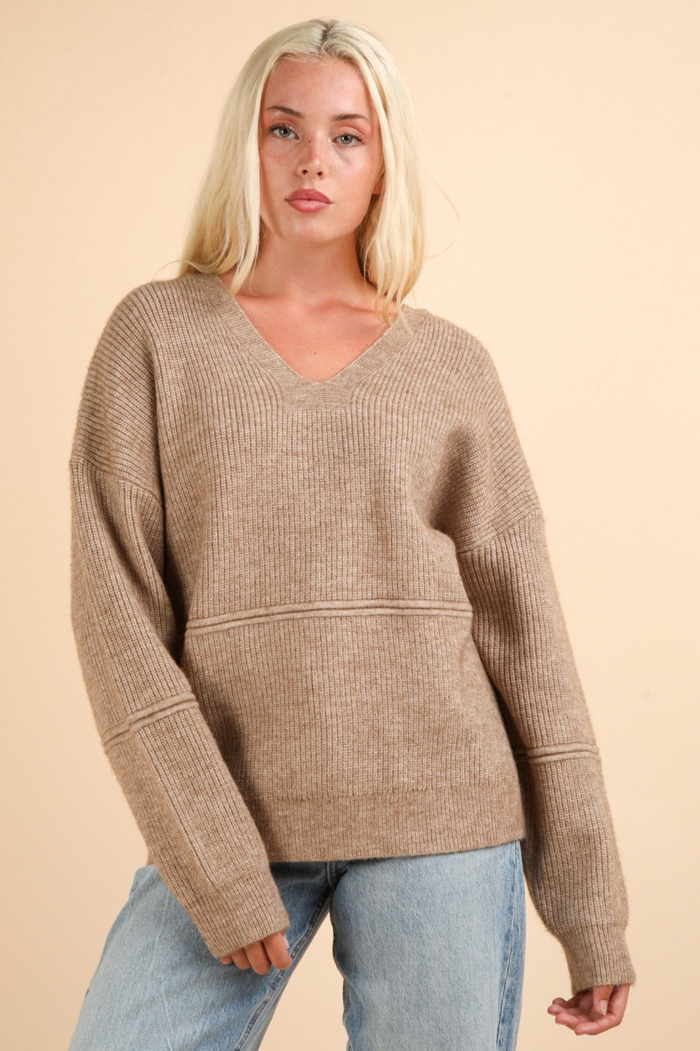 Woman wearing a beige ribbed knit drop shoulder sweater with seam detail and slightly stretchy fabric composition of 95% cotton, 5% spandex.