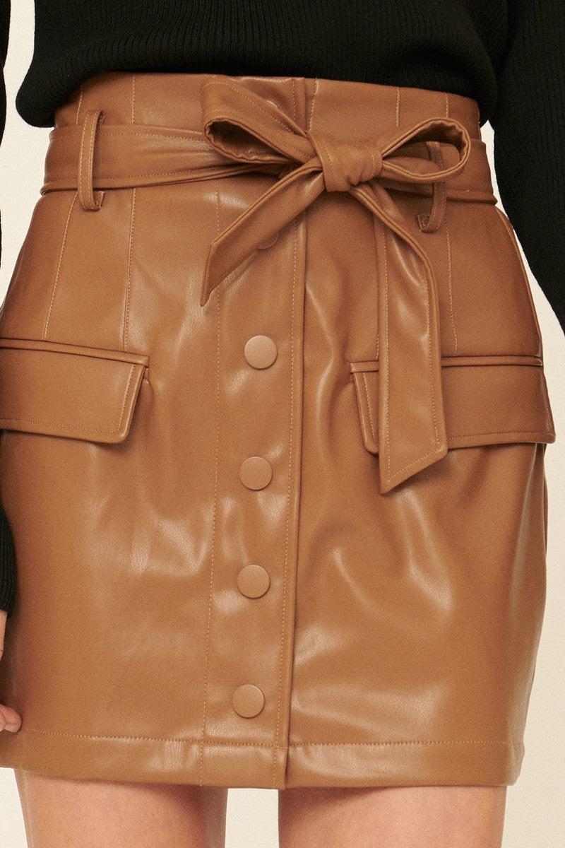 Camel faux leather mini skirt with removable self-tie belt, button closure, decorative pocket flaps, and smocked elastic back.