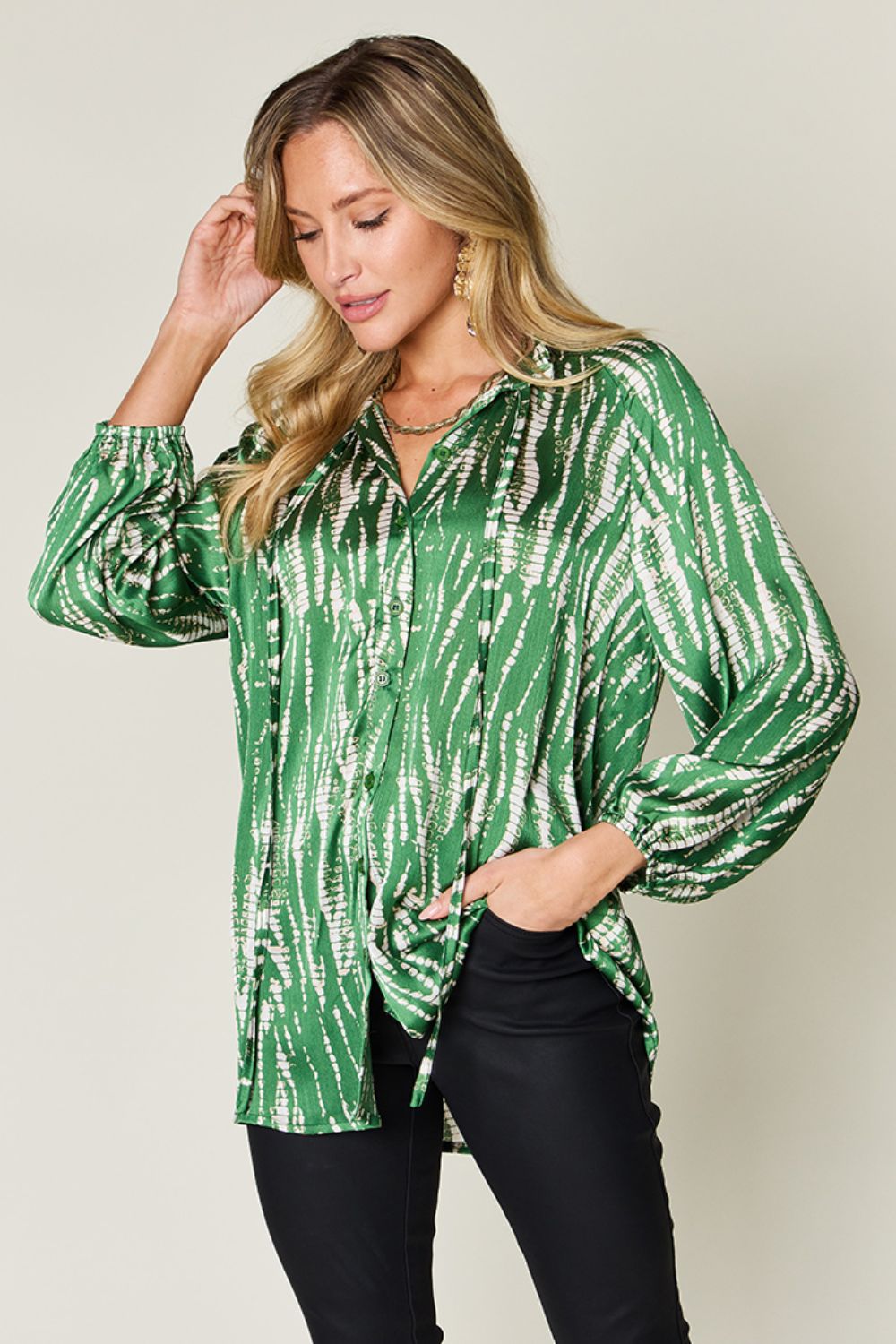 Woman wearing a green printed button-up long sleeve shirt made of 100% polyester with frill detailing, paired with black pants.