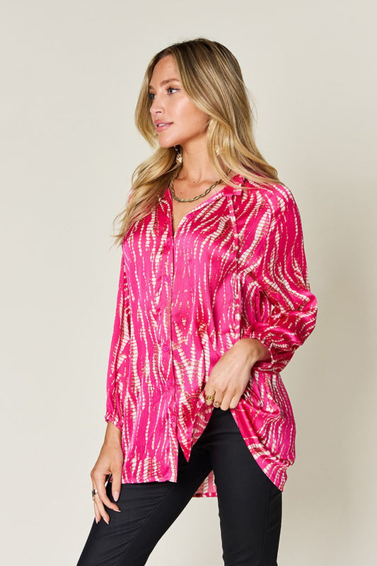 Woman wearing a pink printed button-up long sleeve shirt with frills, made of 100% polyester, and styled with black pants.