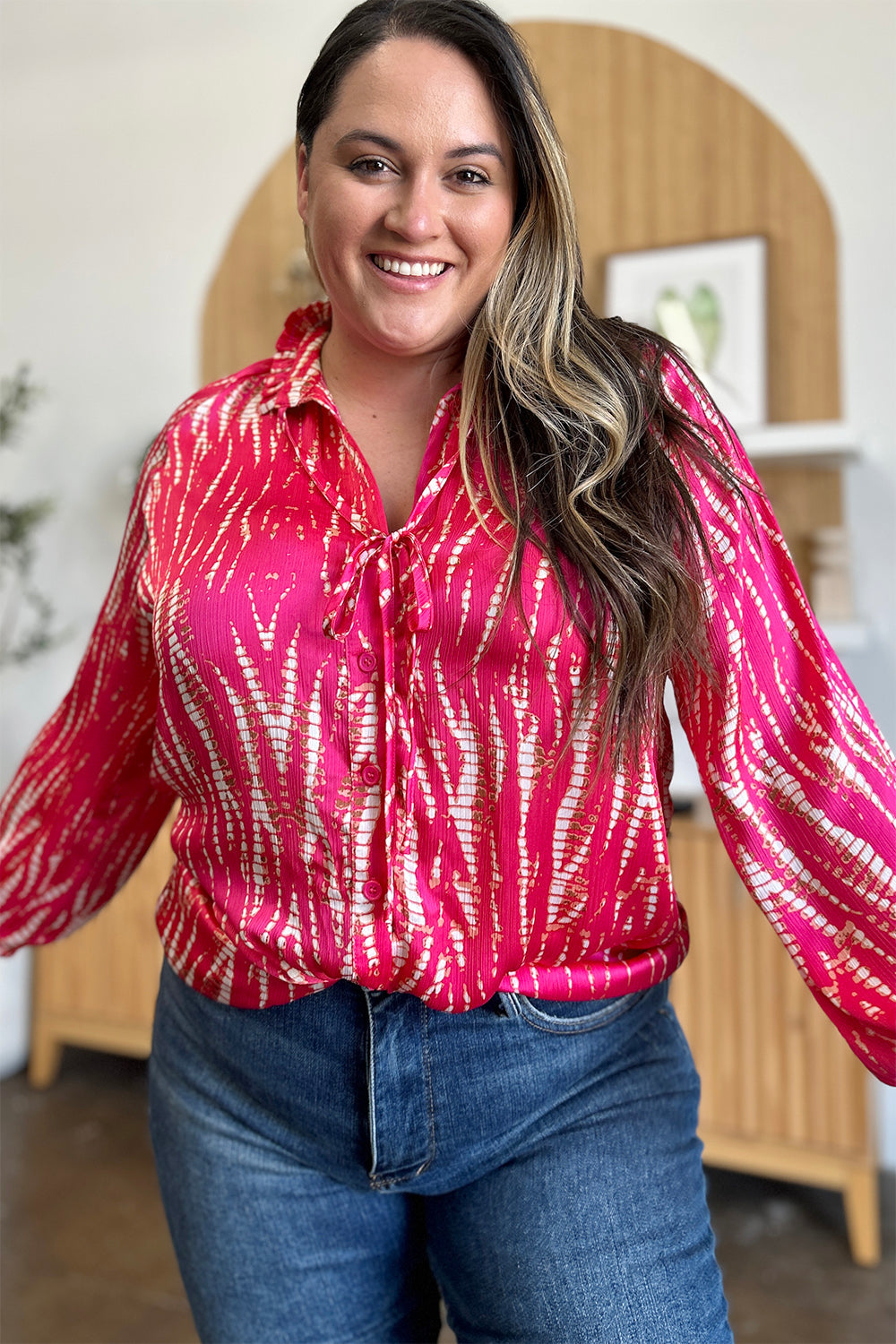 Woman wearing a printed button up long sleeve shirt in vibrant pink and red pattern, perfect for casual or office wear.