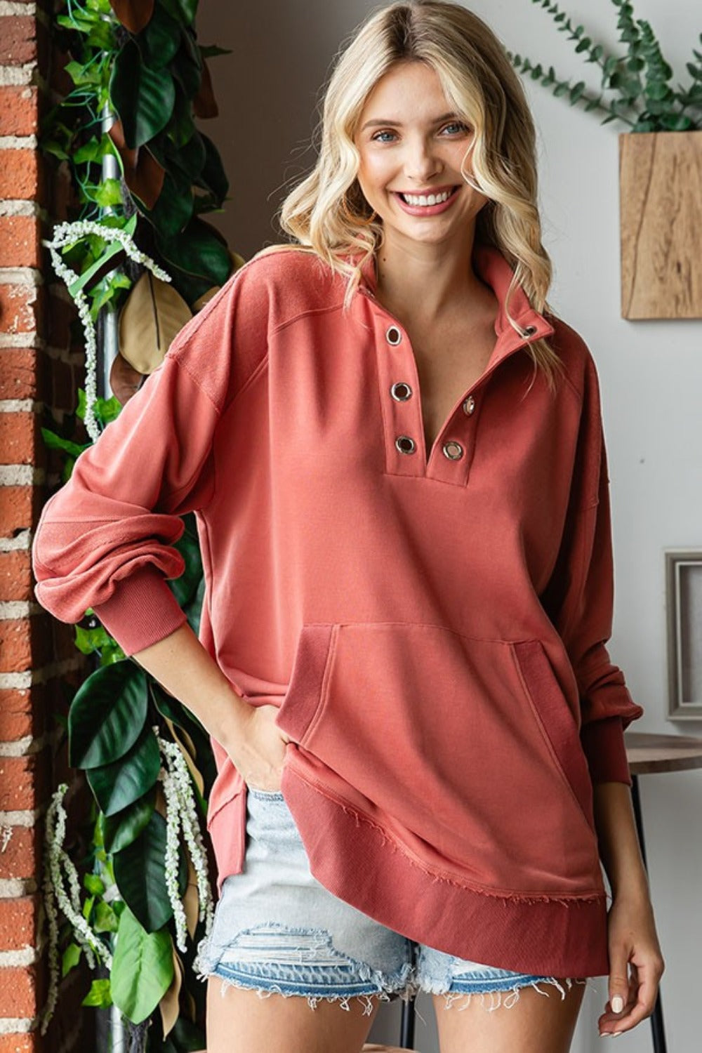 Woman wearing a grommet split neck kangaroo pocket sweatshirt in coral, with a casual look and raw hem design.