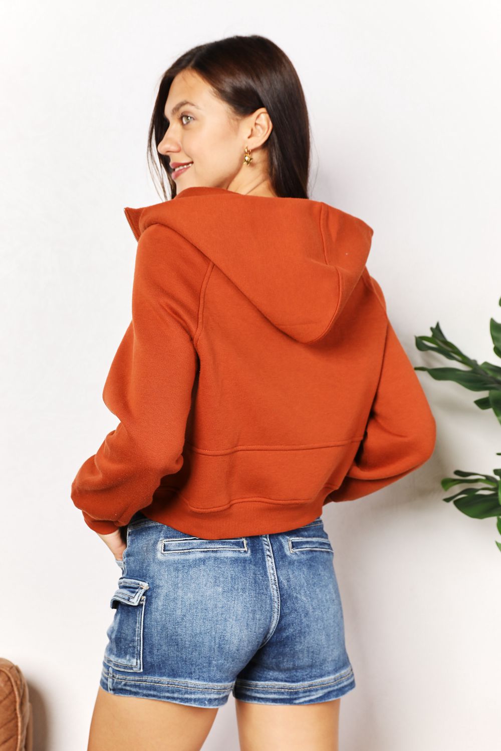 Chic half-zip long sleeve hoodie in solid rust, featuring ribbed collared neck and raglan sleeves, paired with denim shorts.