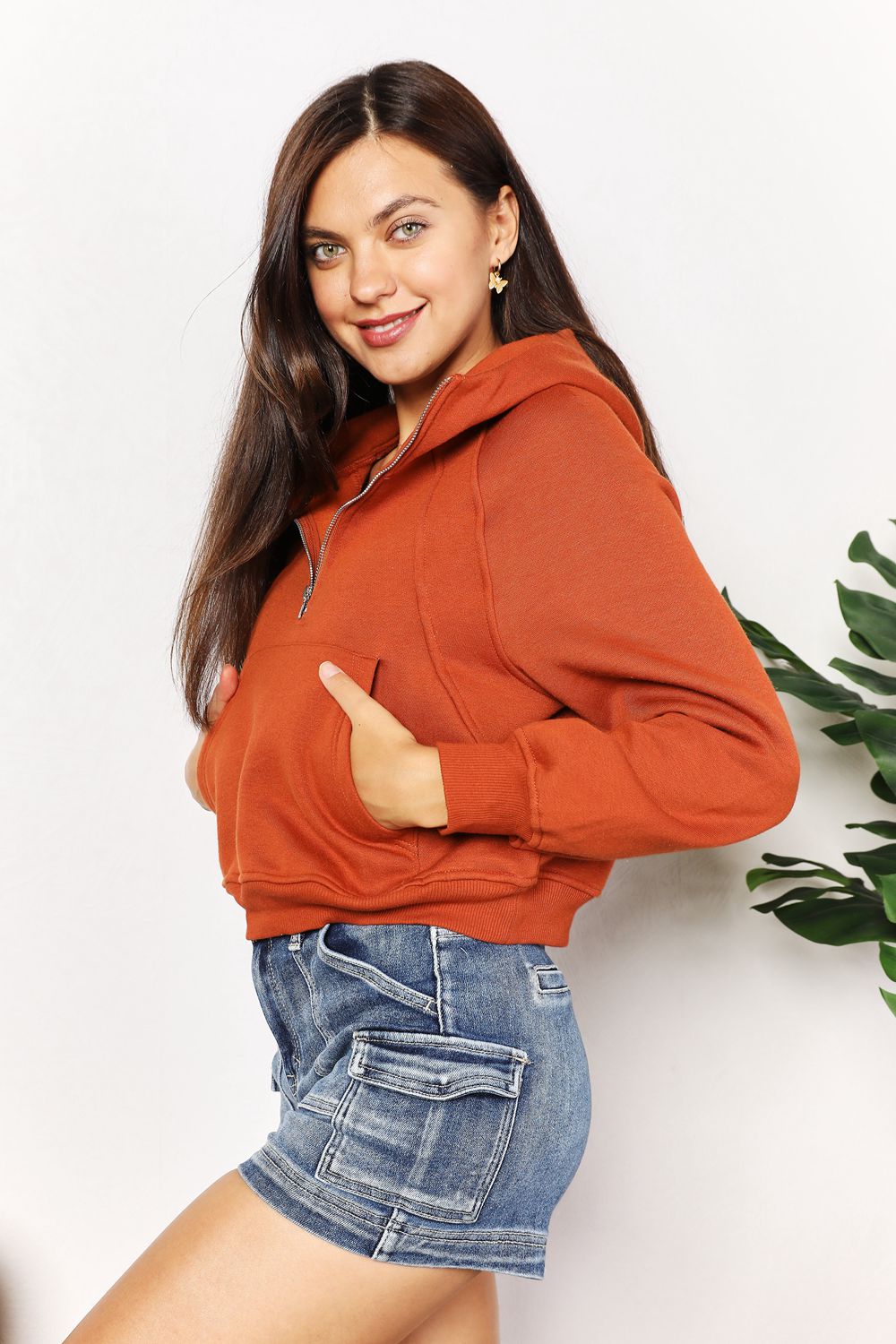 Woman wearing chic half-zip long sleeve hoodie with solid pattern, collared neck, and raglan sleeves, paired with denim shorts.