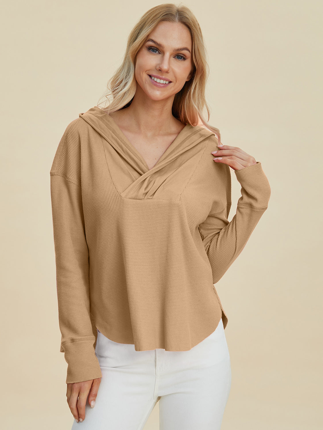 Woman wearing a high-low dropped shoulder long sleeve hoodie in beige, showcasing its slightly stretchy fit and polyester-cotton blend.