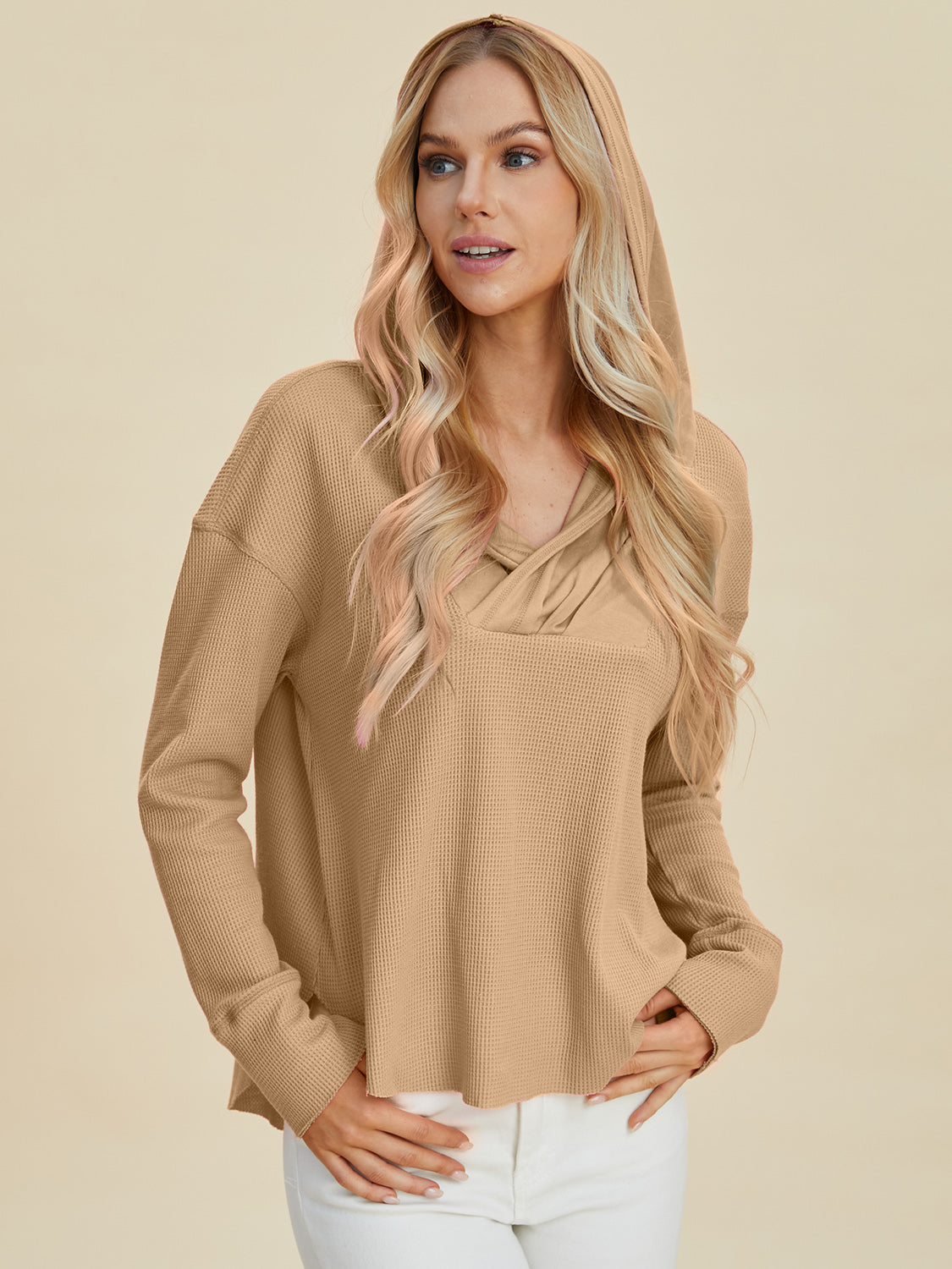 Woman wearing high-low dropped shoulder long sleeve hoodie in beige, slightly stretchy, made of polyester and cotton.