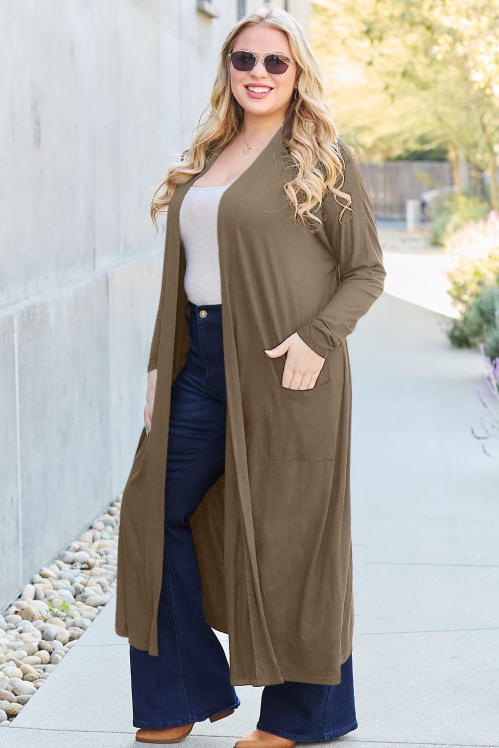 Woman wearing open front long sleeve cover up with pockets, stylishly paired with jeans, outdoors on a sunny day.