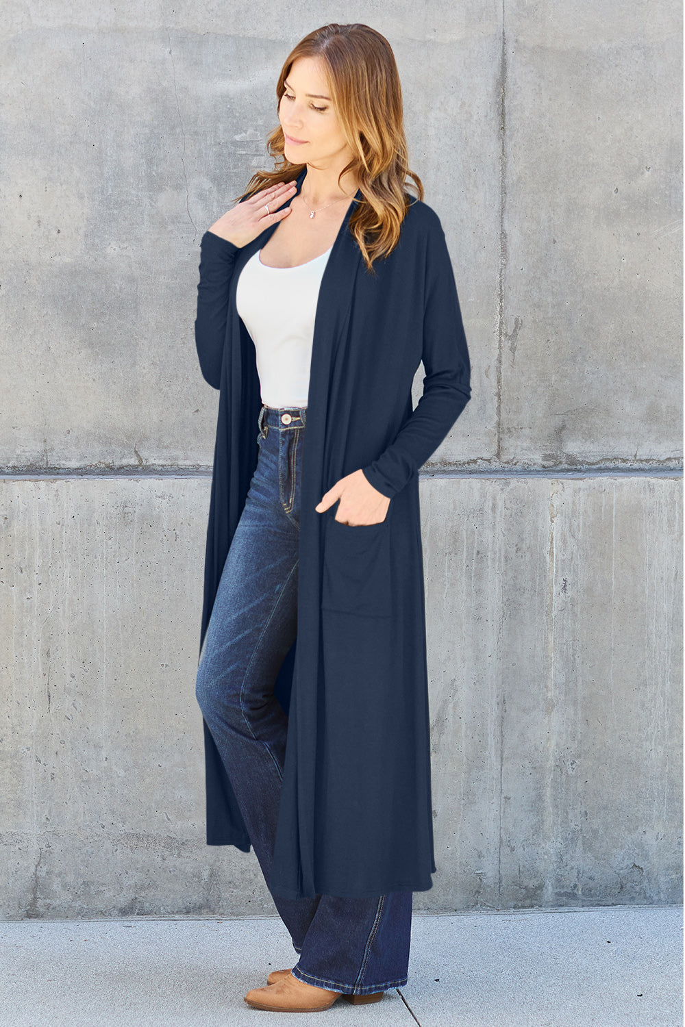 Woman wearing open front long sleeve cover up with pockets, styled over a white top and blue jeans.