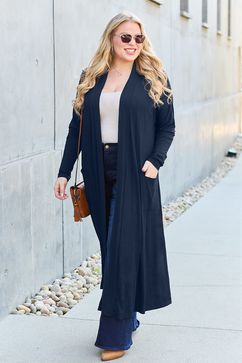 Woman wearing open front long sleeve cover up with pockets, styled with jeans and sunglasses, casual street look.