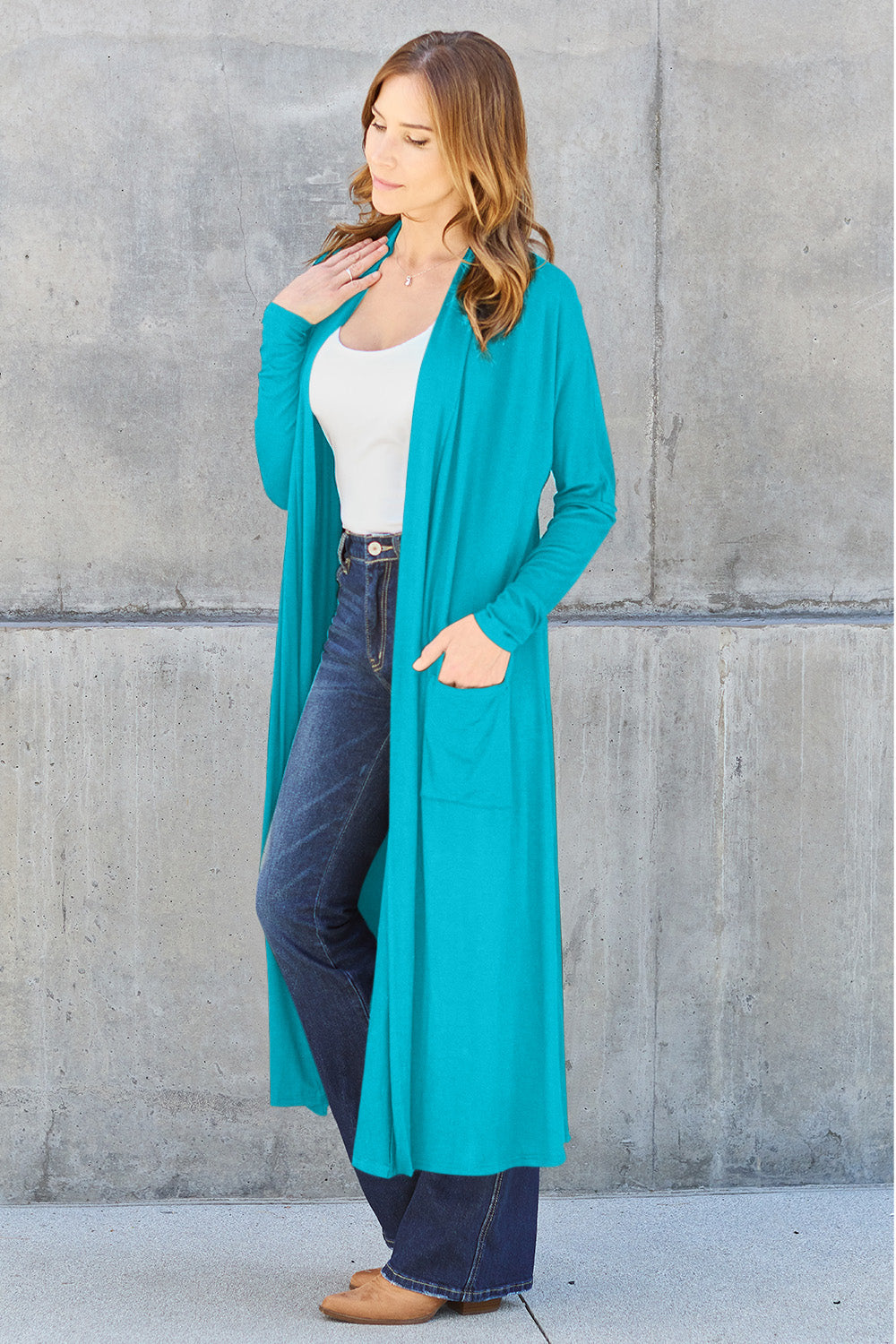 Woman wearing teal open front long sleeve cover up with pockets over jeans