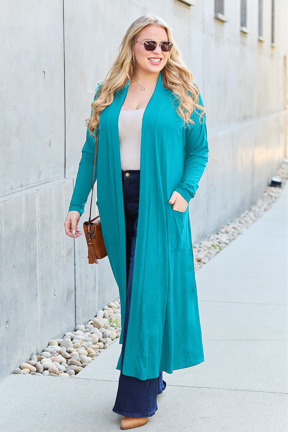 Woman wearing teal open front long sleeve cover up with pockets, paired with sunglasses and casual outfit.