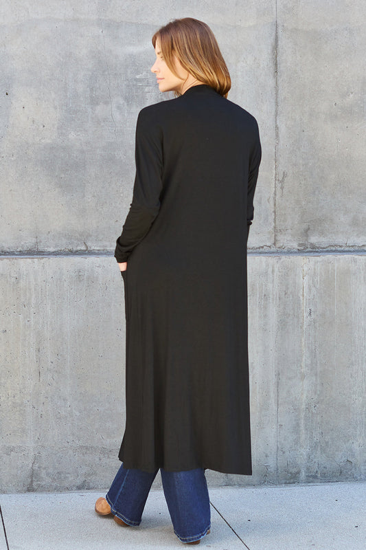 Woman wearing black open front long sleeve cover up with pockets, paired with jeans.