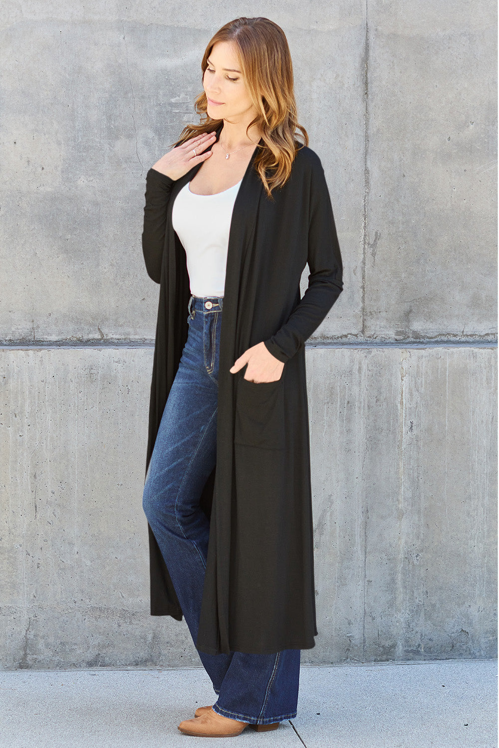 Woman wearing a black open front long sleeve cover up with pockets, paired with jeans and a white top.