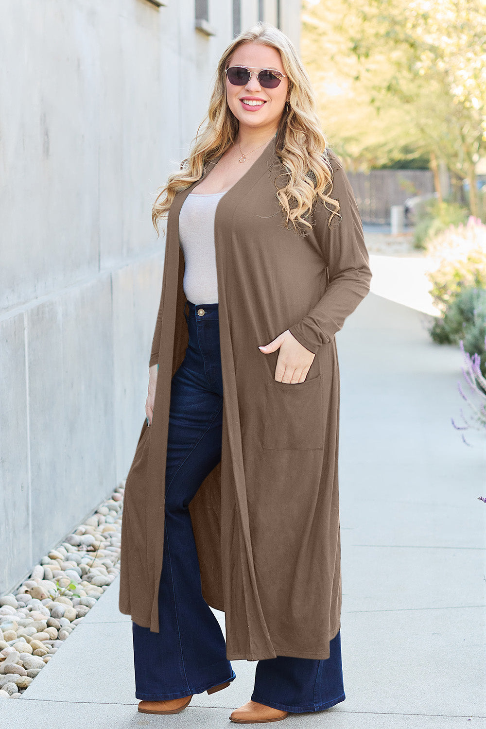 Woman wearing open front long sleeve cover up with pockets paired with jeans and sunglasses.