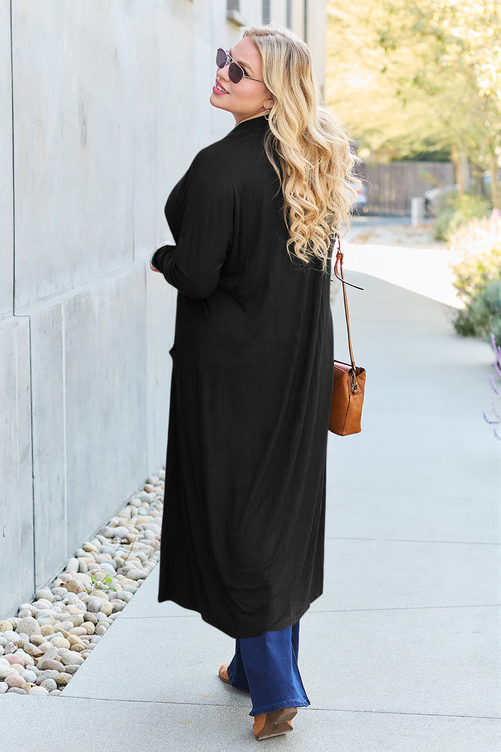 Woman wearing long sleeve open front cover up with pockets, paired with jeans and sunglasses, walking outdoors.