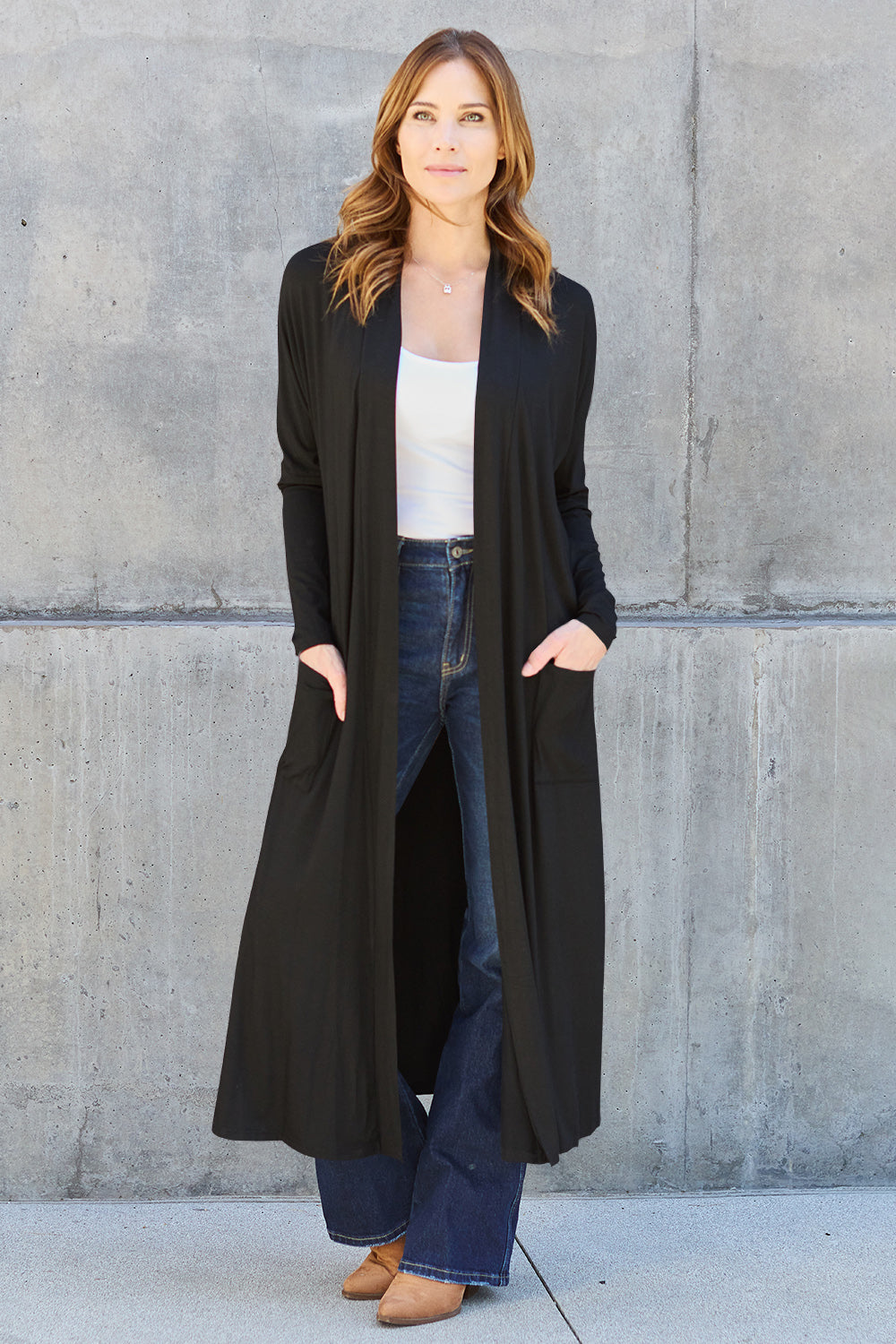 Woman wearing long black open front cover up with pockets over casual outfit.