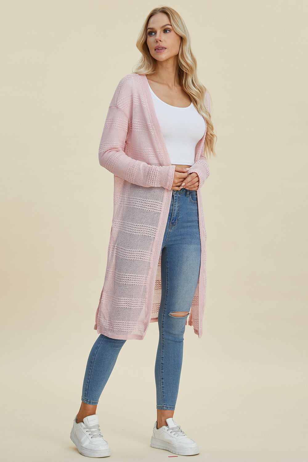 Woman wearing a pink open front longline cardigan with openwork design and moderate stretch, paired with jeans and a white top