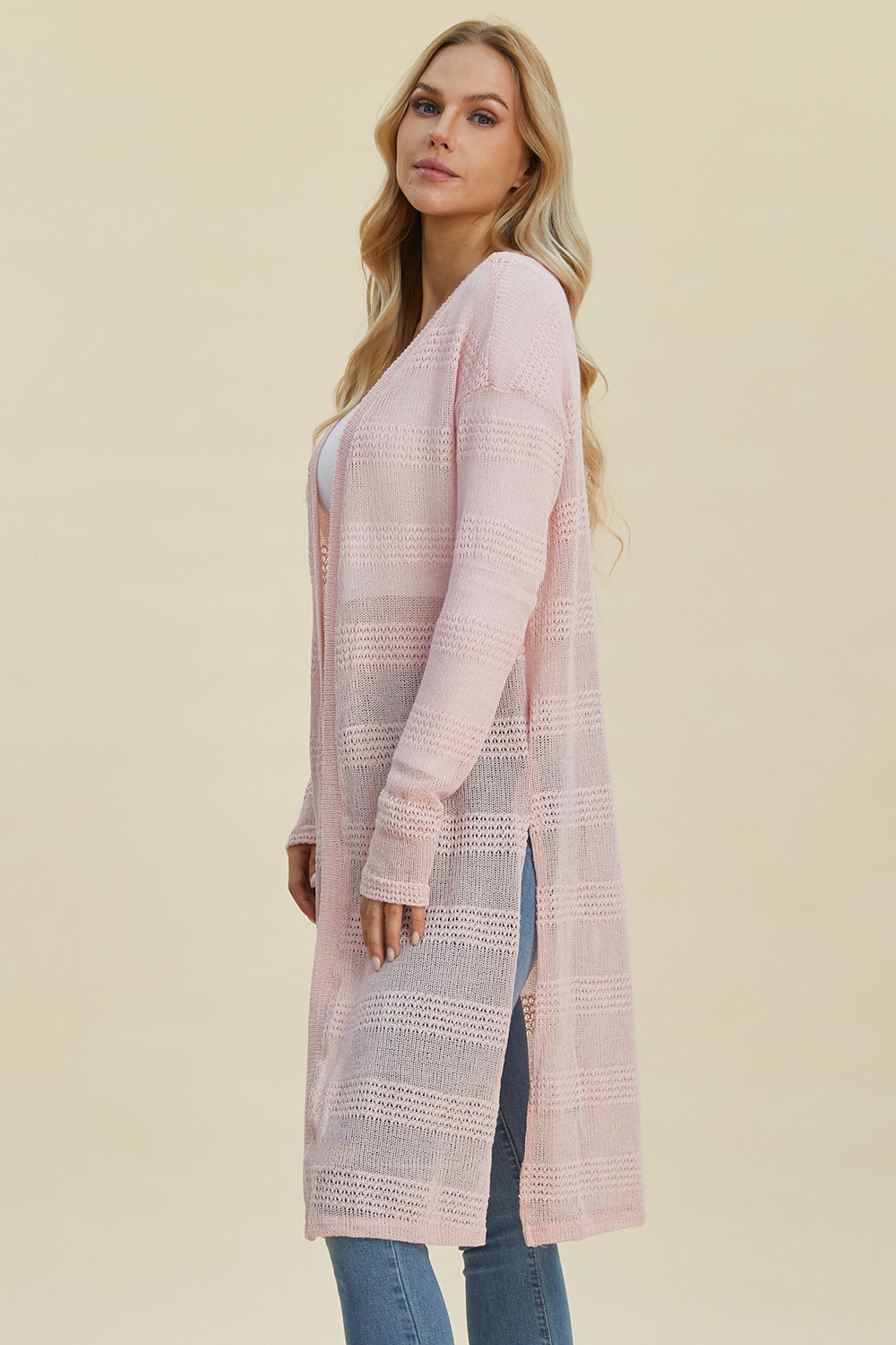 Woman wearing a pink open front longline cardigan with an openwork design, made of 100% polyester, offering moderate stretch.