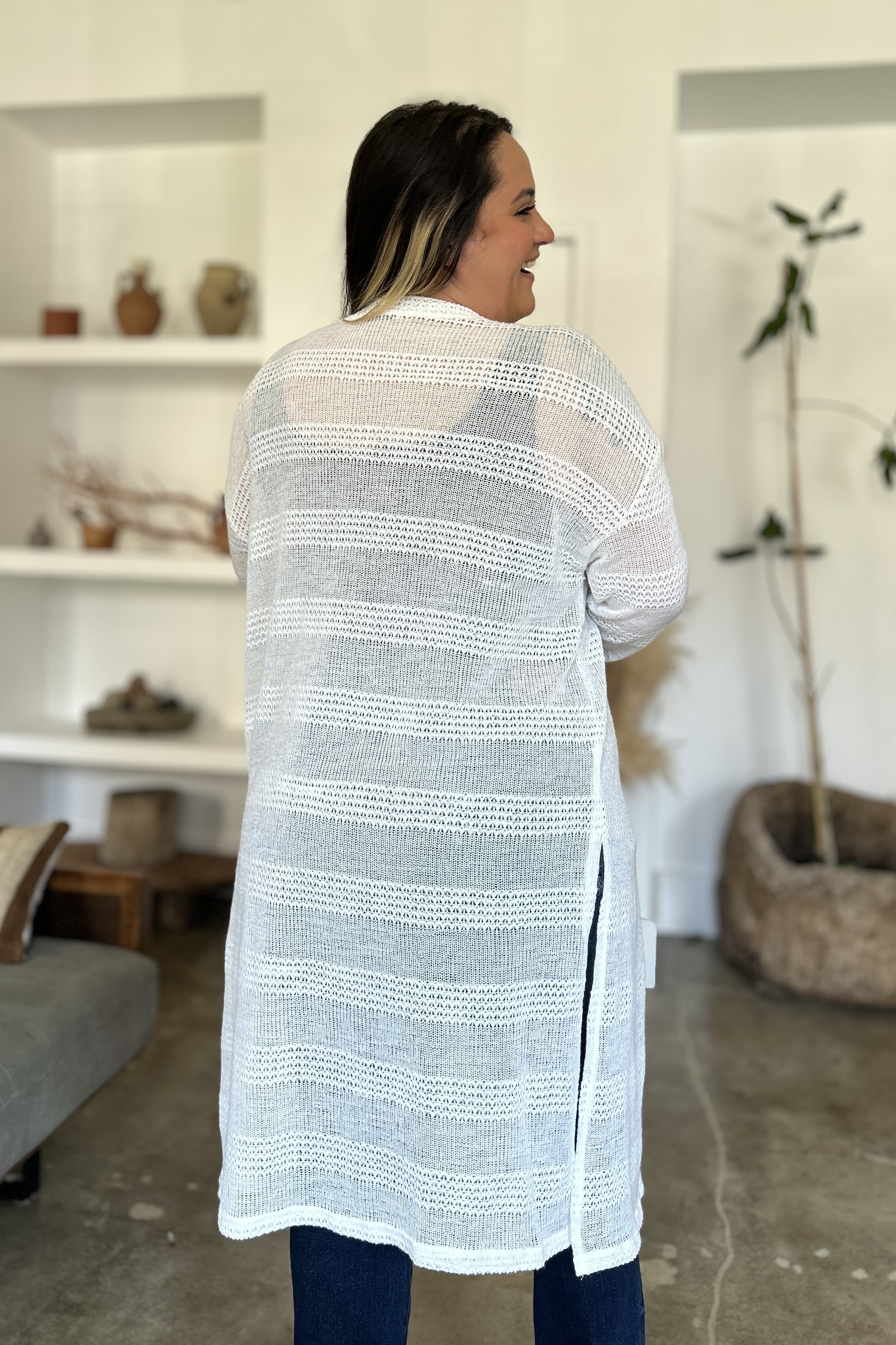 Woman wearing openwork longline cardigan with open front, moderate stretch, and 100% polyester material in modern indoor setting.