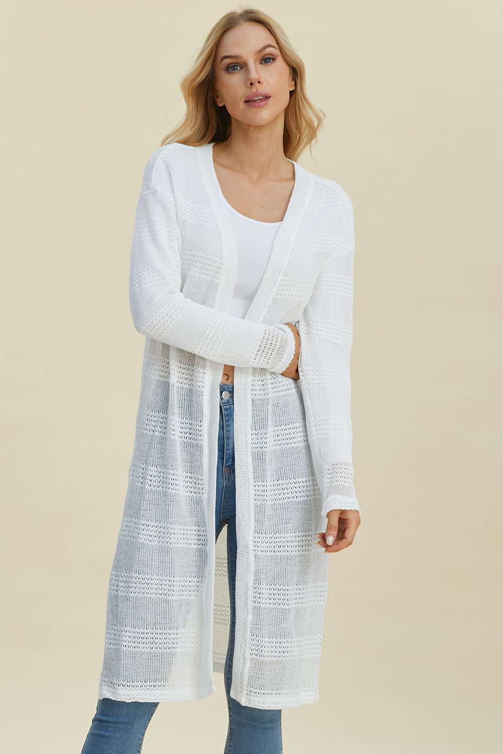 Woman wearing white open front longline cardigan with openwork design, featuring moderate stretch and 100% polyester material.