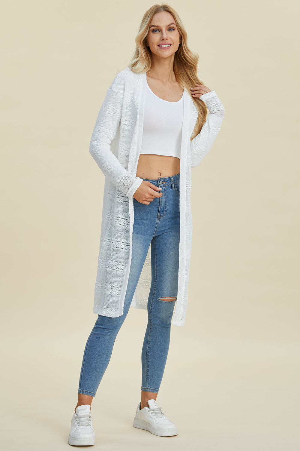 Woman wearing a stylish open front longline cardigan with openwork design, paired with jeans and a white top, showcasing a chic casual look.