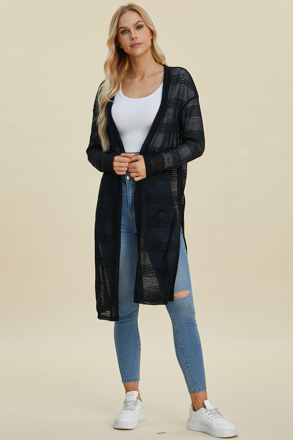 Woman wearing open front longline black cardigan with moderate stretch and openwork design, paired with jeans and sneakers.