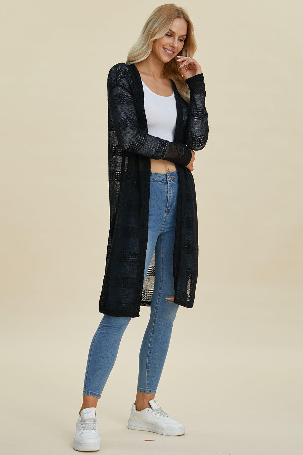 Woman wearing openwork longline cardigan with moderate stretch in black, paired with jeans and sneakers.