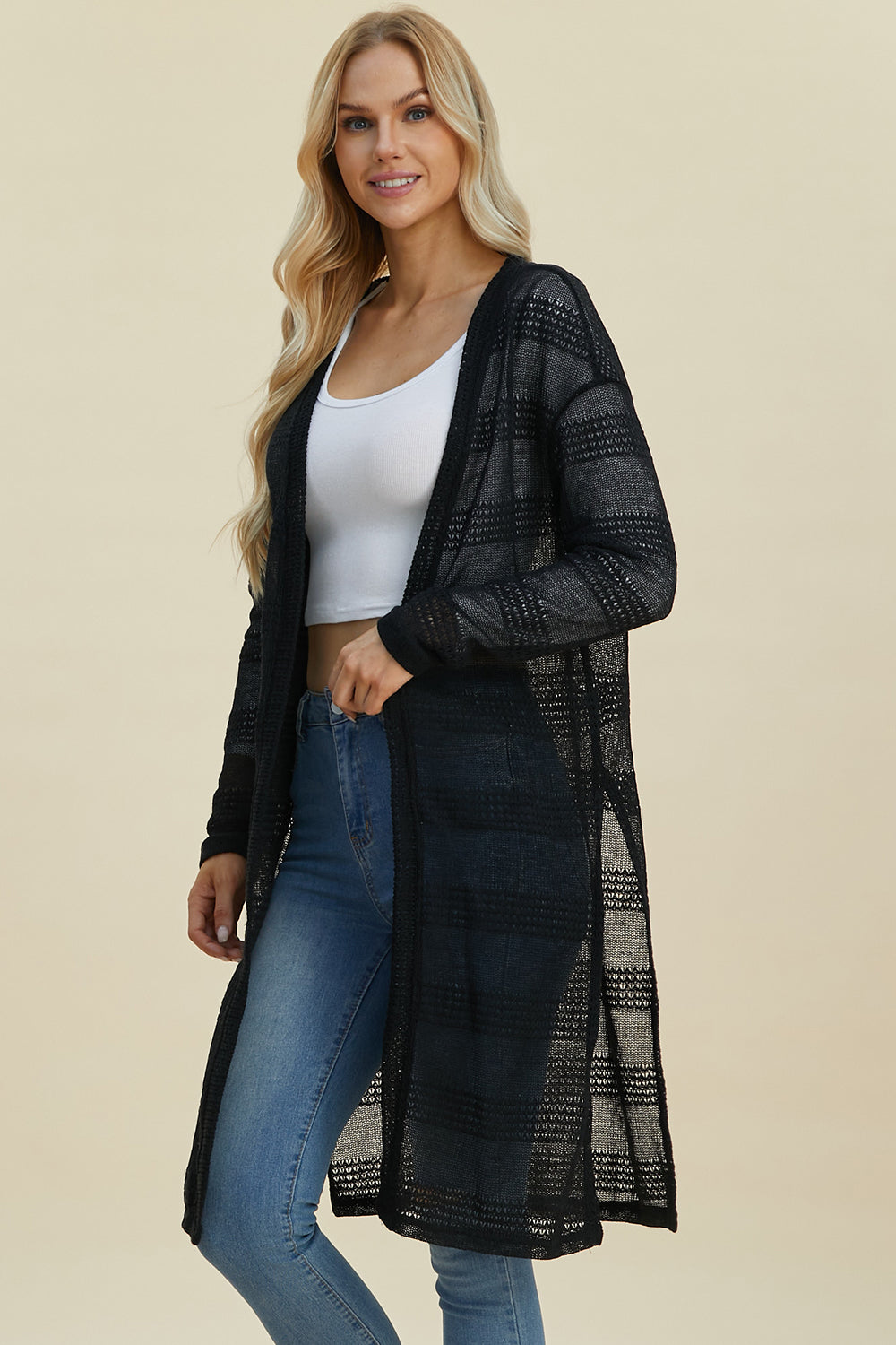 Woman wearing open front longline black cardigan with moderate stretch, layered over a white top and jeans, highlighting openwork design.