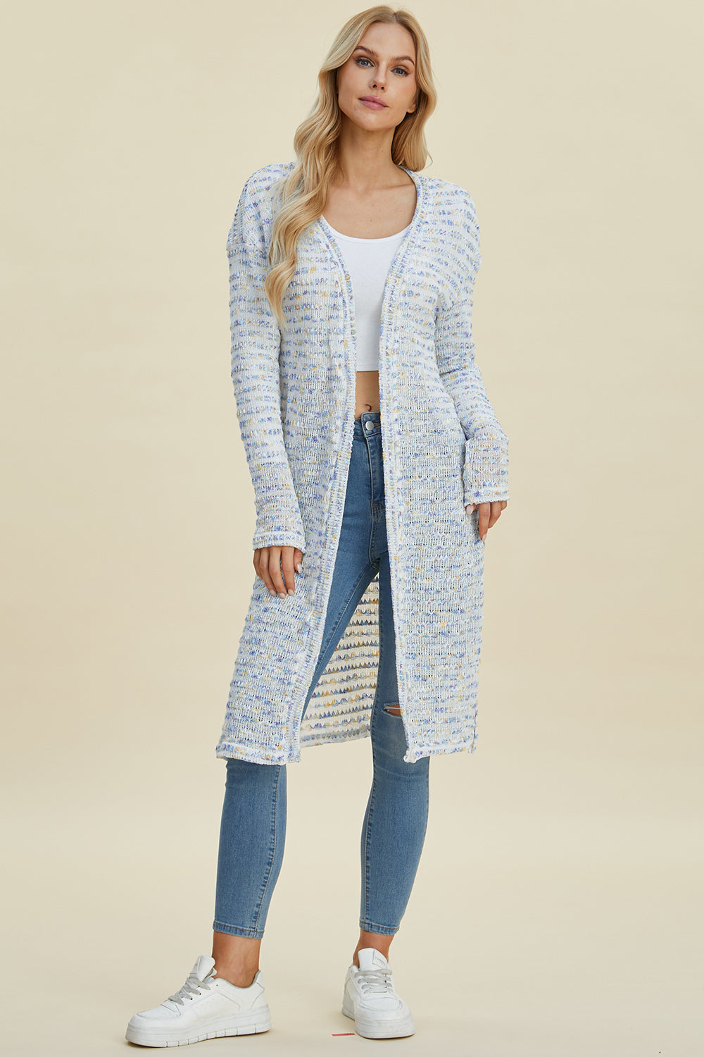 Woman wearing open front longline cardigan with openwork design, moderate stretch, made of 100% polyester, styled with jeans and sneakers.