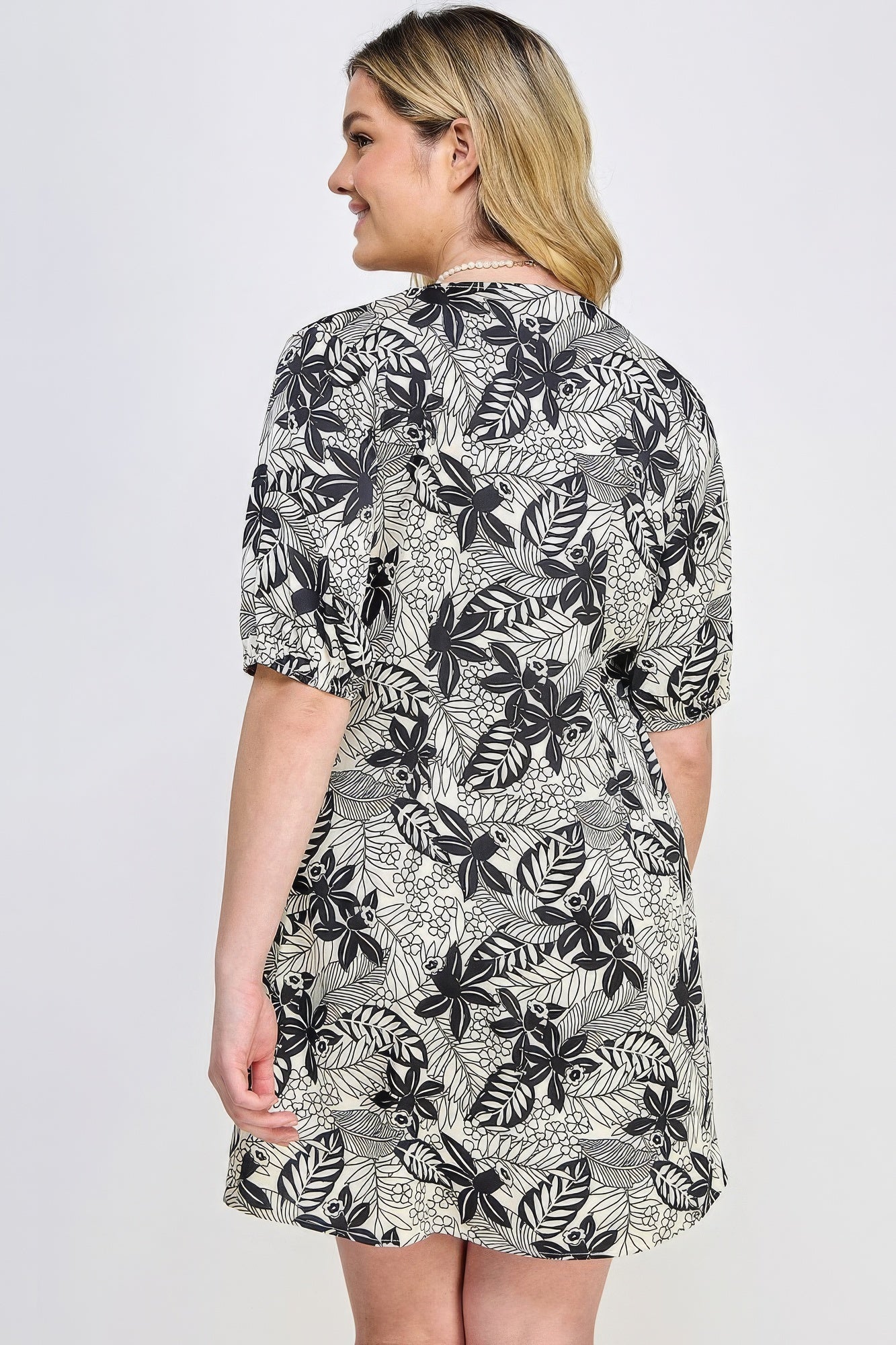 Plus size woman wearing a black botanical print mini dress with front tie, showcasing back view and comfortable fit.