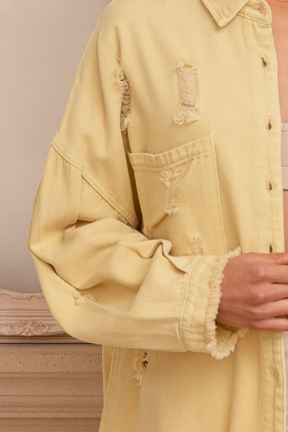 Yellow distressed shacket with raw hem and button-down design made of 100% cotton.