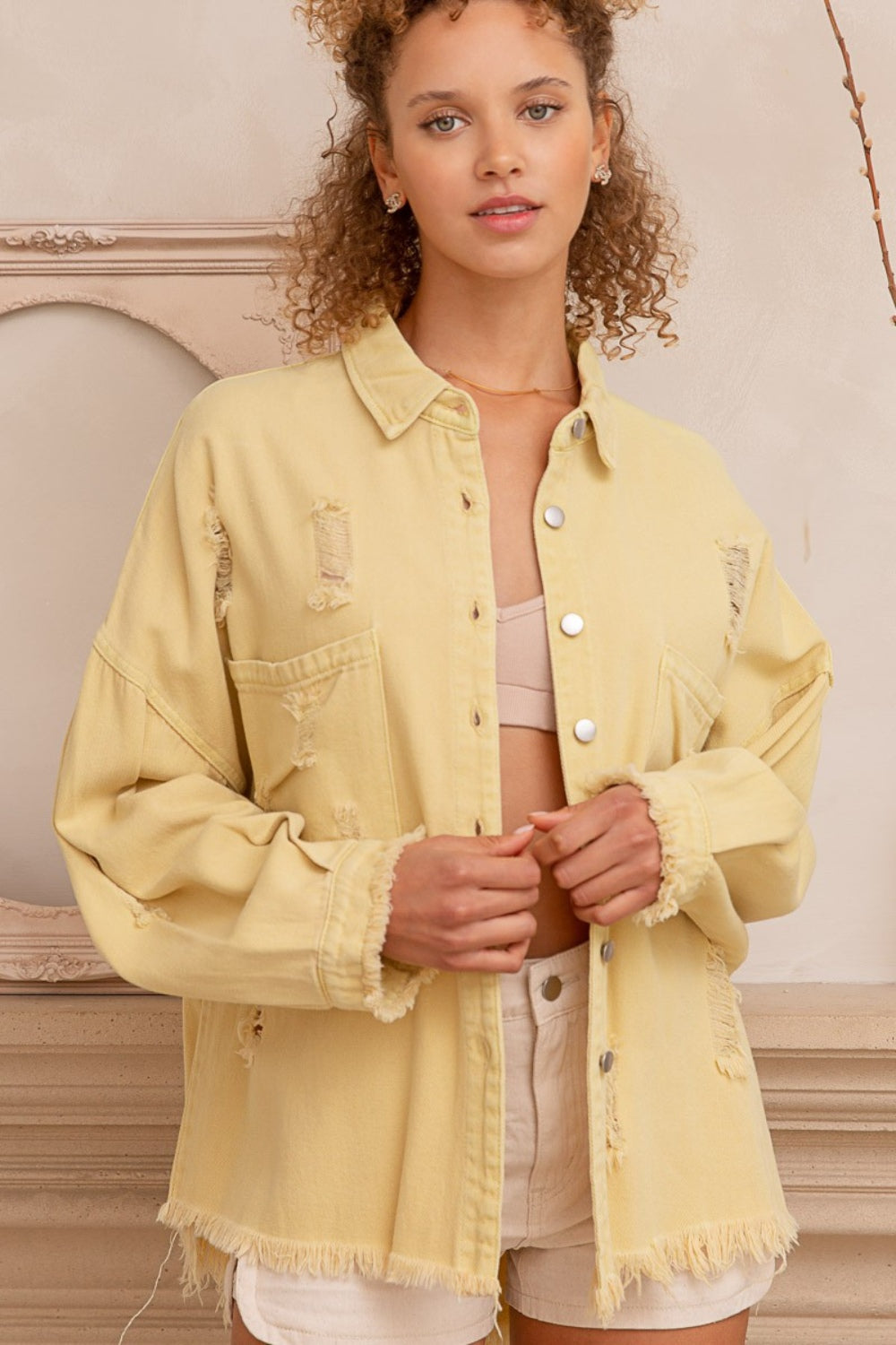 Woman wearing a button-down raw hem distressed shacket made of 100% cotton in light yellow.