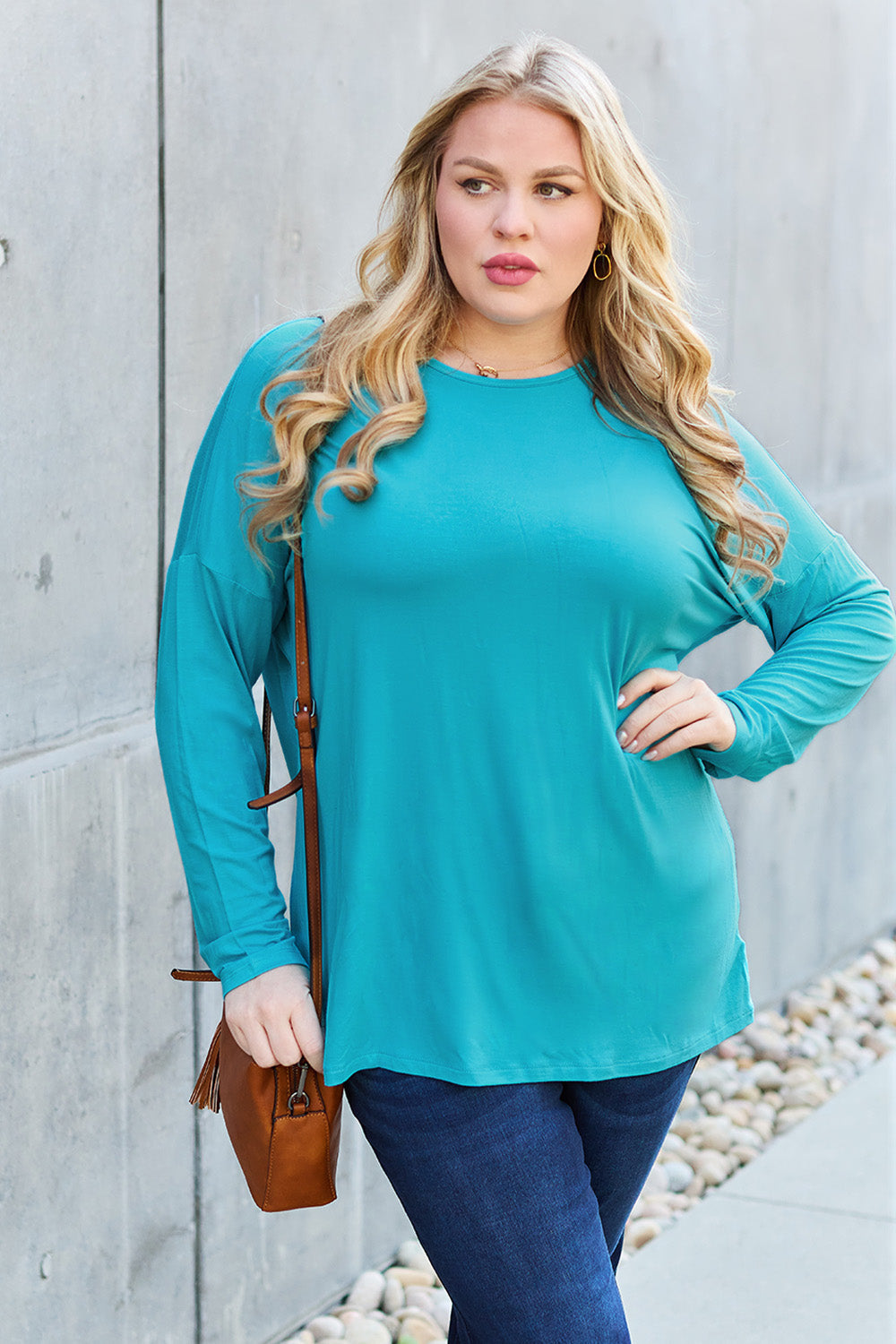 Woman wearing turquoise round neck dropped shoulder t-shirt with jeans and carrying a brown purse.