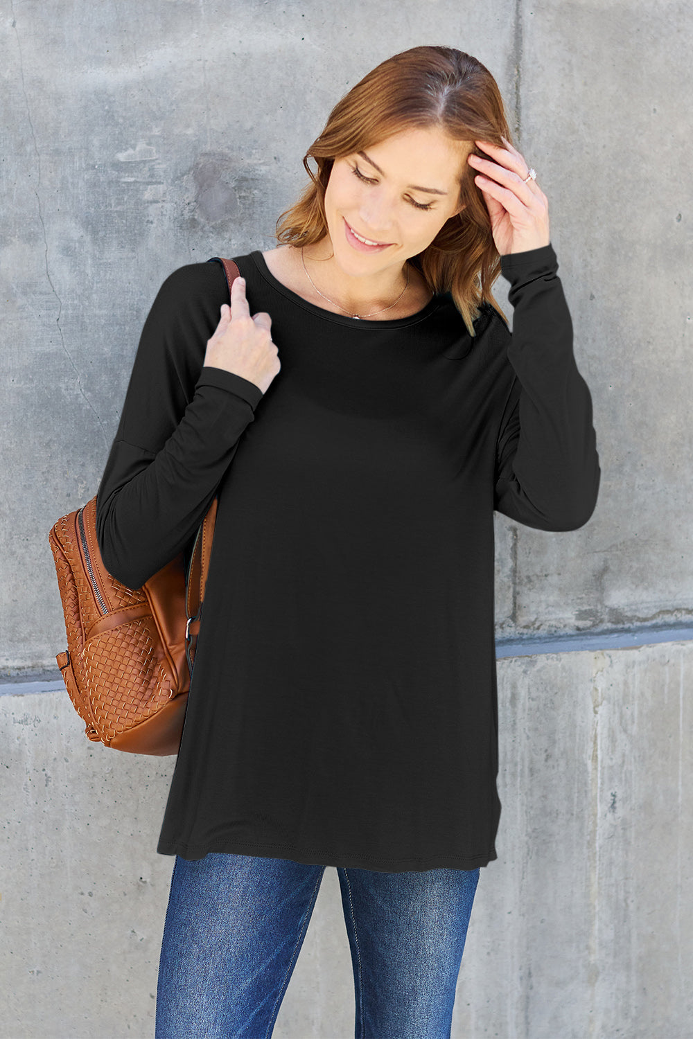 Woman wearing black round neck dropped shoulder t-shirt, paired with jeans and a brown backpack.