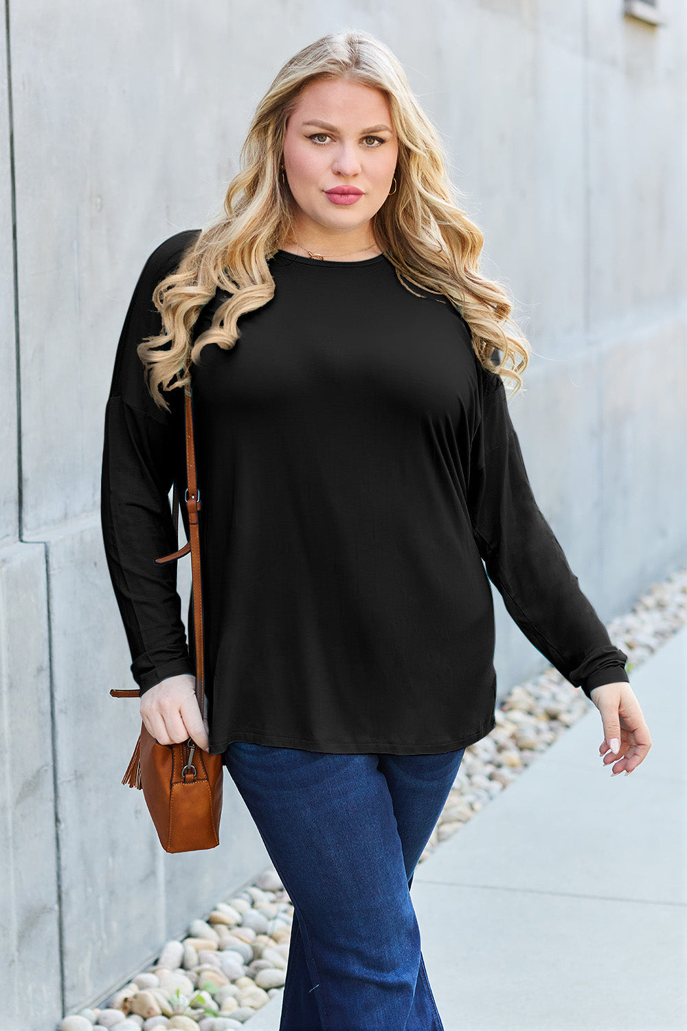 Woman wearing black round neck dropped shoulder t-shirt, paired with blue jeans and brown bag, showcasing a casual style.