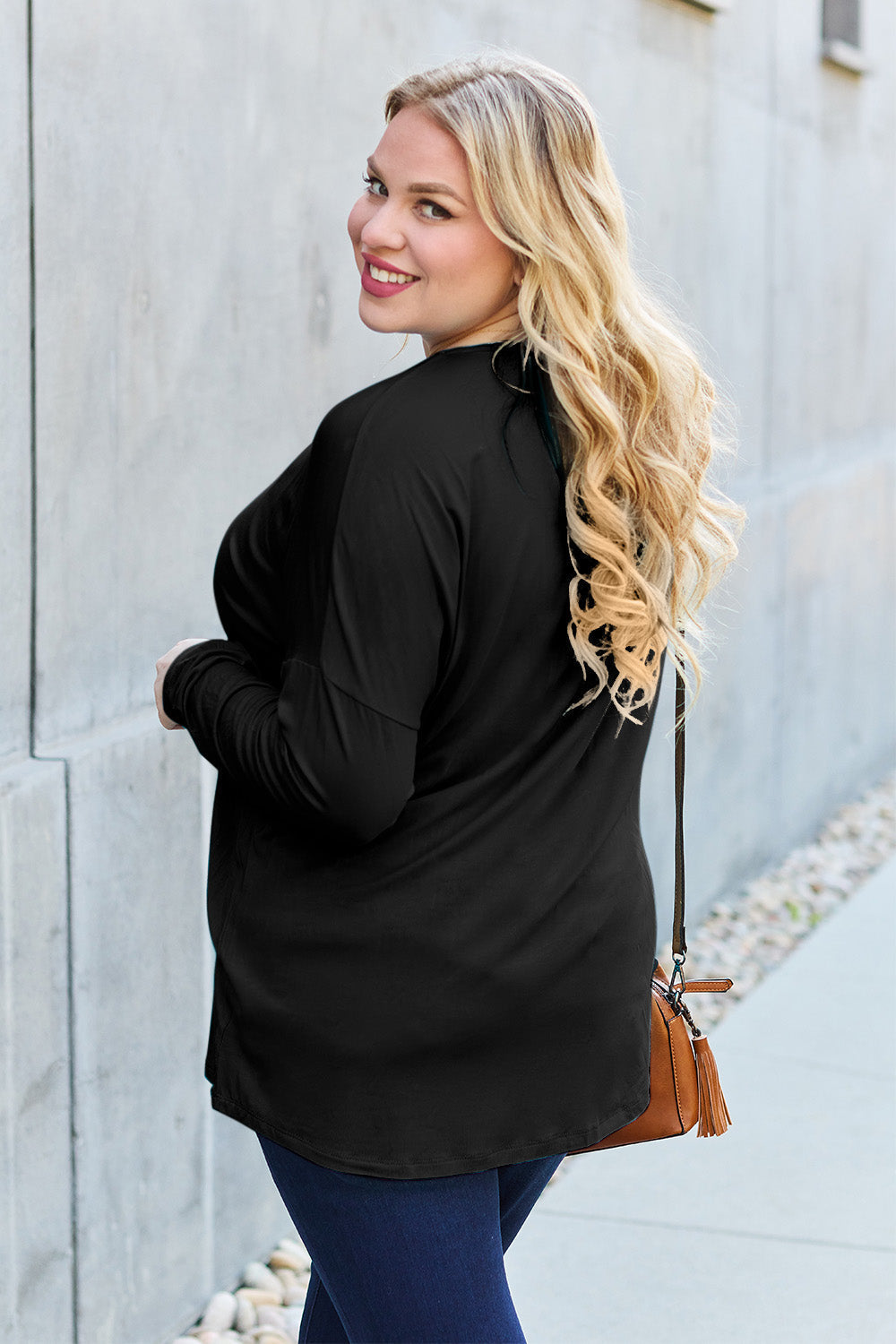 Woman wearing a black round neck dropped shoulder t-shirt, styled with blue jeans and a small brown crossbody bag.