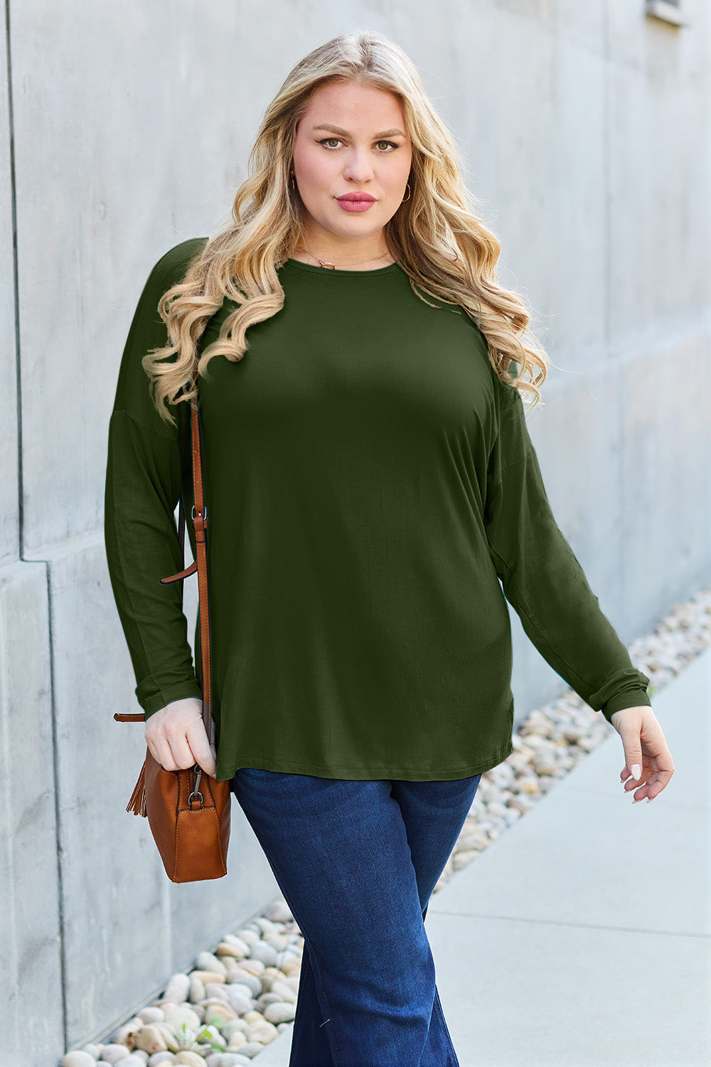 Woman wearing a round neck dropped shoulder T-shirt in green with slightly stretchy fabric, paired with blue jeans and a brown bag.