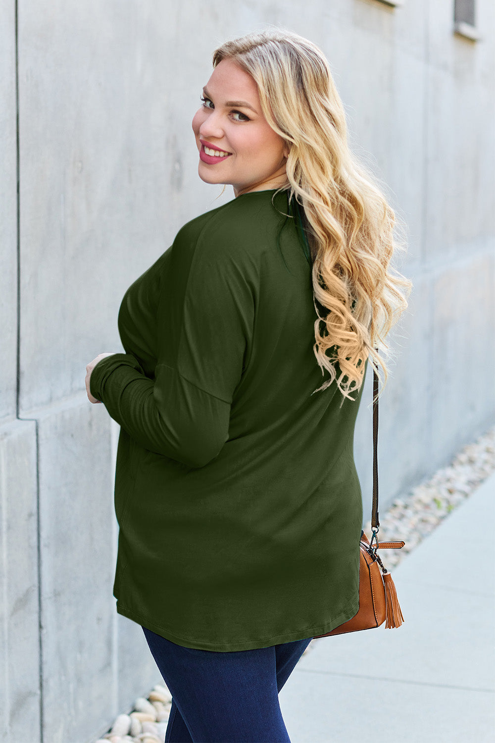 Woman wearing an olive green round neck dropped shoulder t-shirt with a relaxed fit, paired with jeans and a crossbody bag.