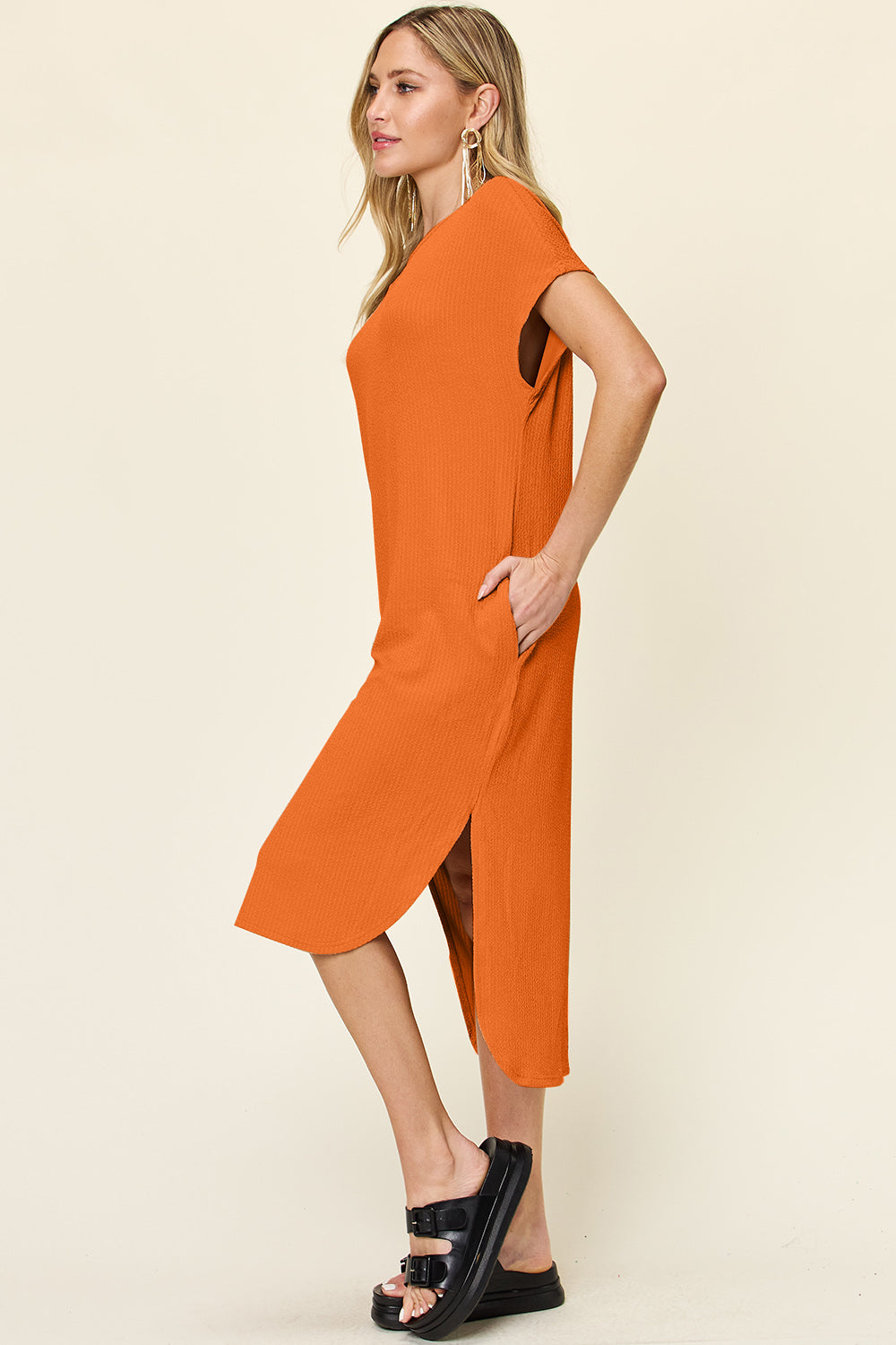 Woman wearing orange round neck short sleeve slit dress with slight stretch, side view.