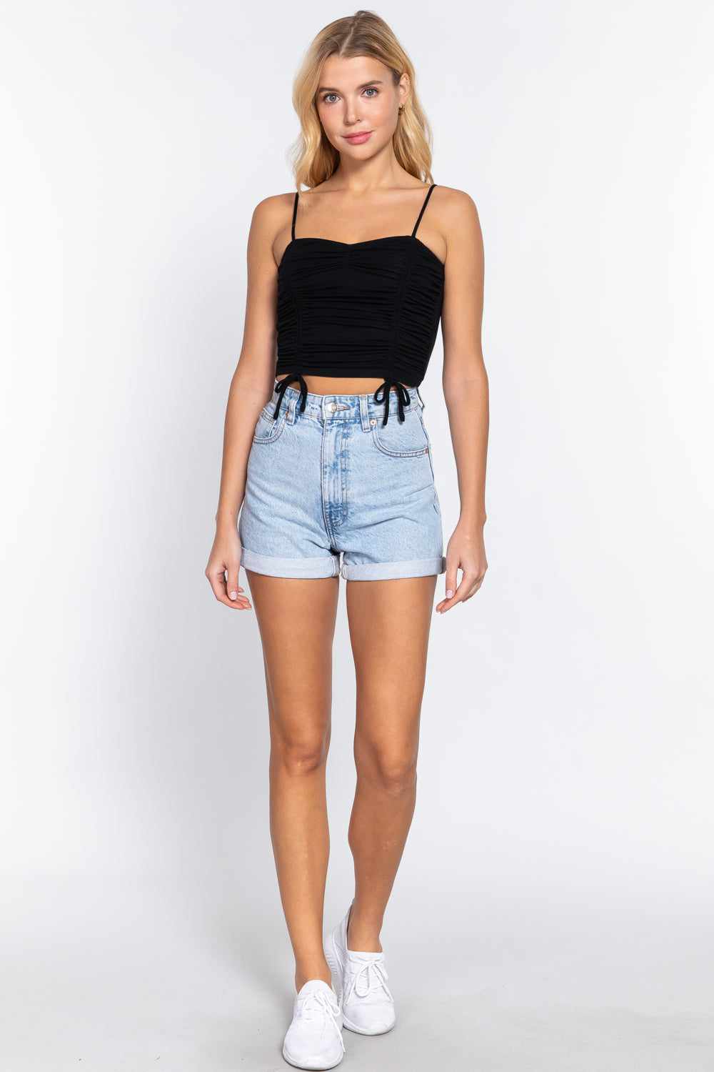 Woman wearing black ruched side shirring cami top paired with denim shorts and white sneakers.